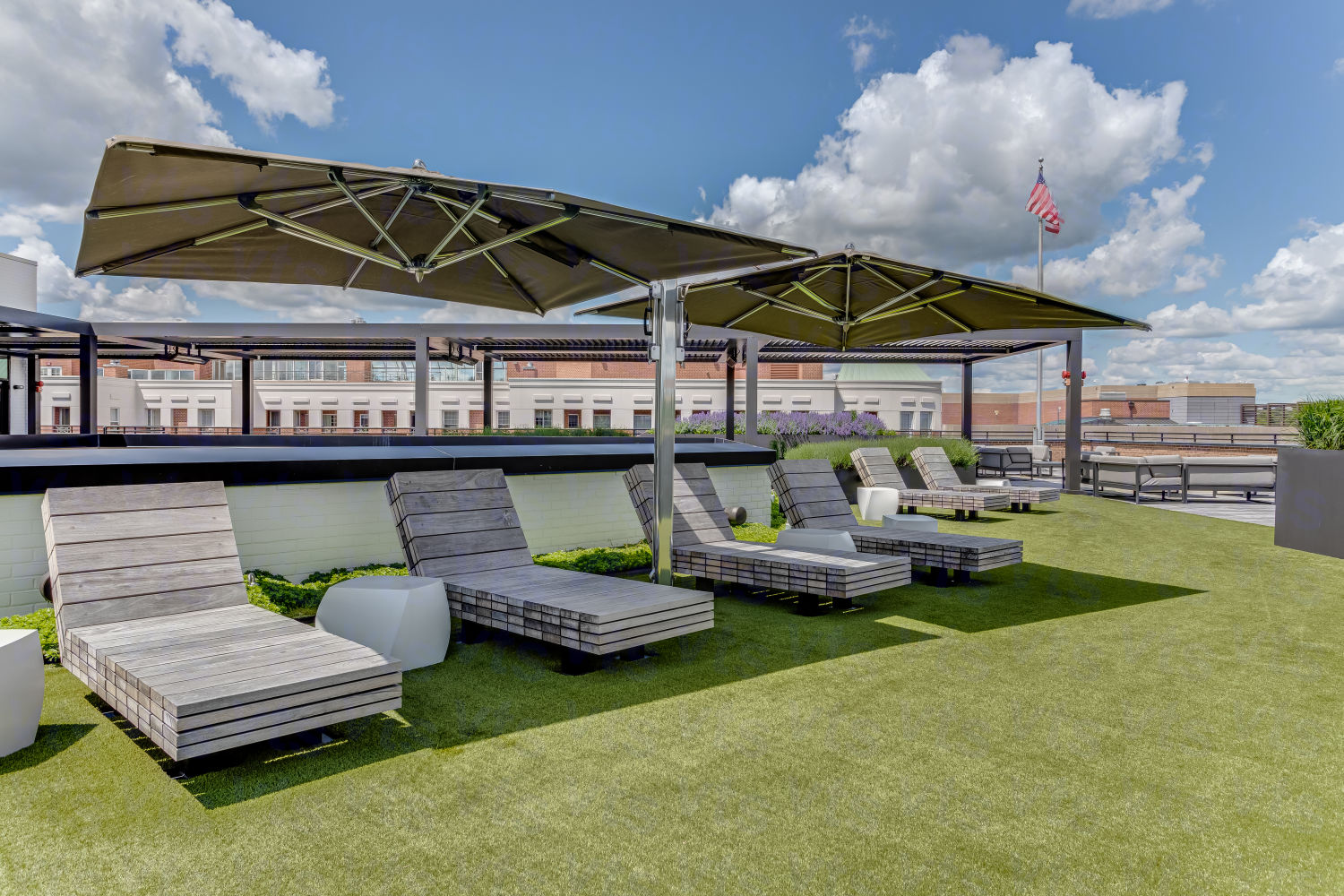 A rooftop lounging area with wooden lounging long-chairs shaded by large expandable umbrellas