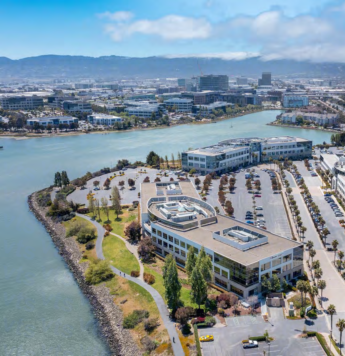 An aerial view of a group of buildings with a park and walkways connecting to an inner parking lot aligned along the waterfont