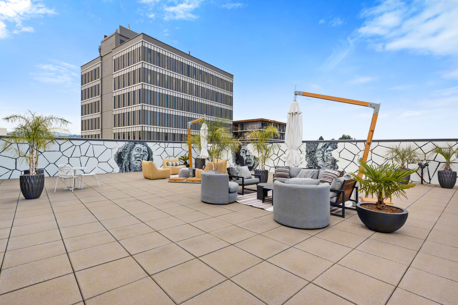 A communal outdoor space with lounge chairs arranged around coffee tables under collapsable hanging umbrellas in the forefront of wall murals 