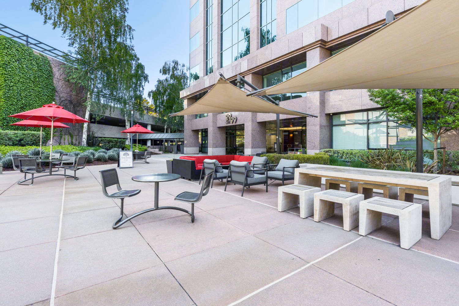 A communal outdoor space next to the building entrance with lounge chairs and sofas under hanging flat unbrellas