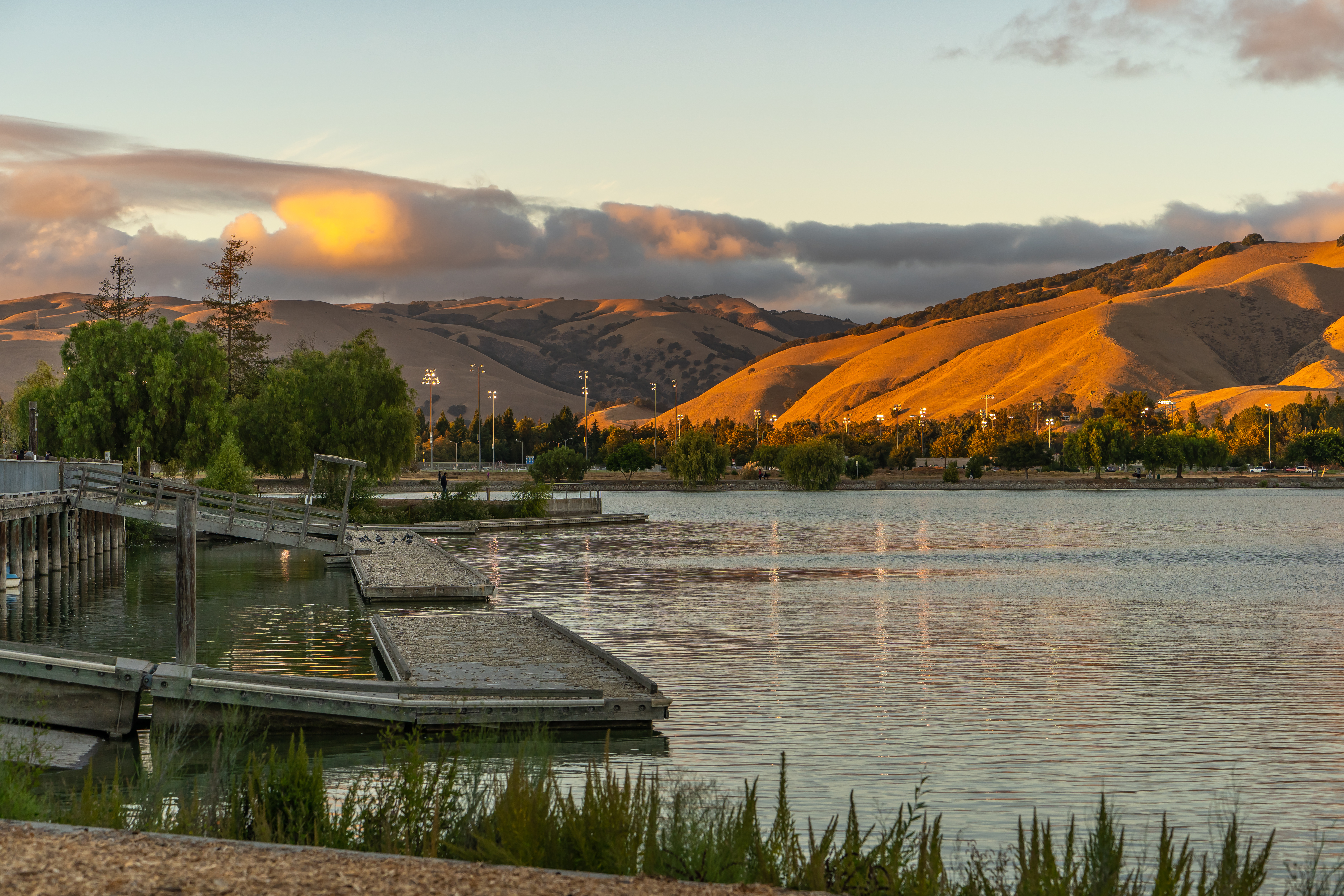 A loading dock next to open water with large hills in the background during a golden hour sunset