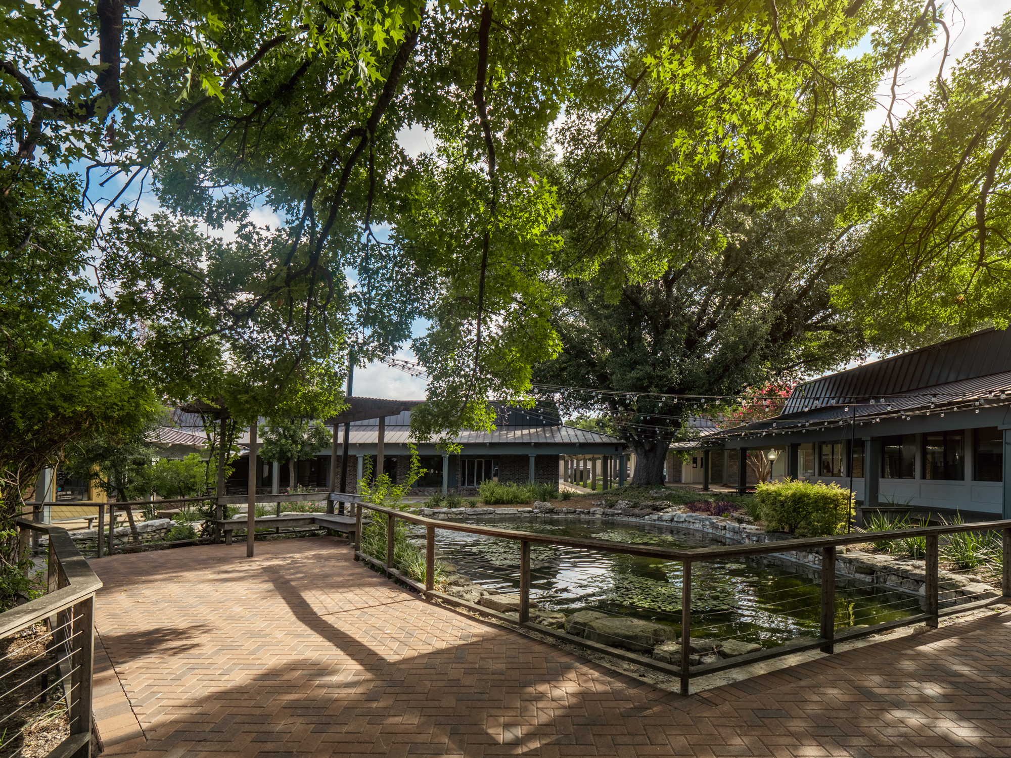 An outdoor patio deck encompassing a koi pond underneath hanging lights and trees